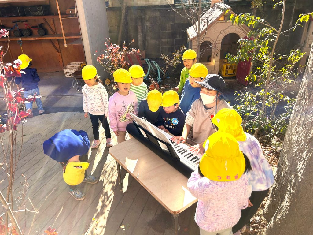園庭でピアノを演奏する先生とこどもたち