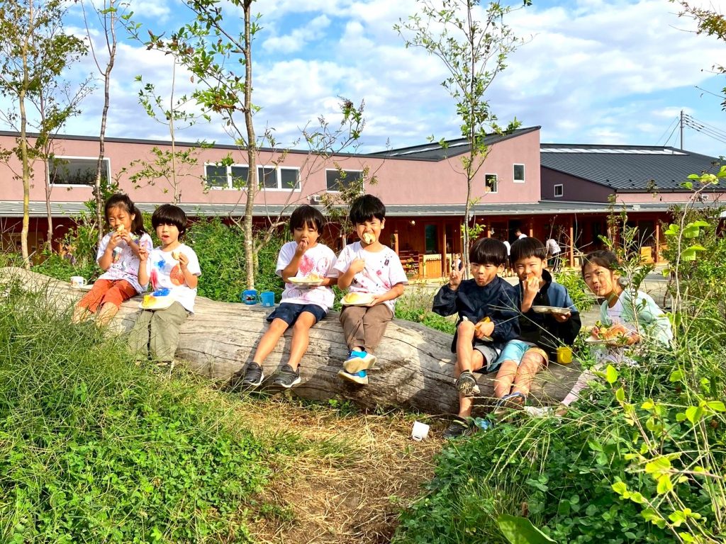 自然豊かな園庭で、丸太に座るこどもたち
